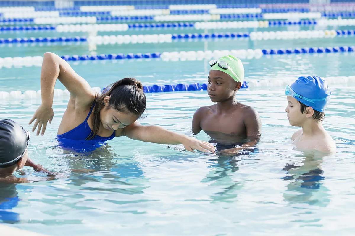 Kids are receiving swim lessons in a pool from an instructor.