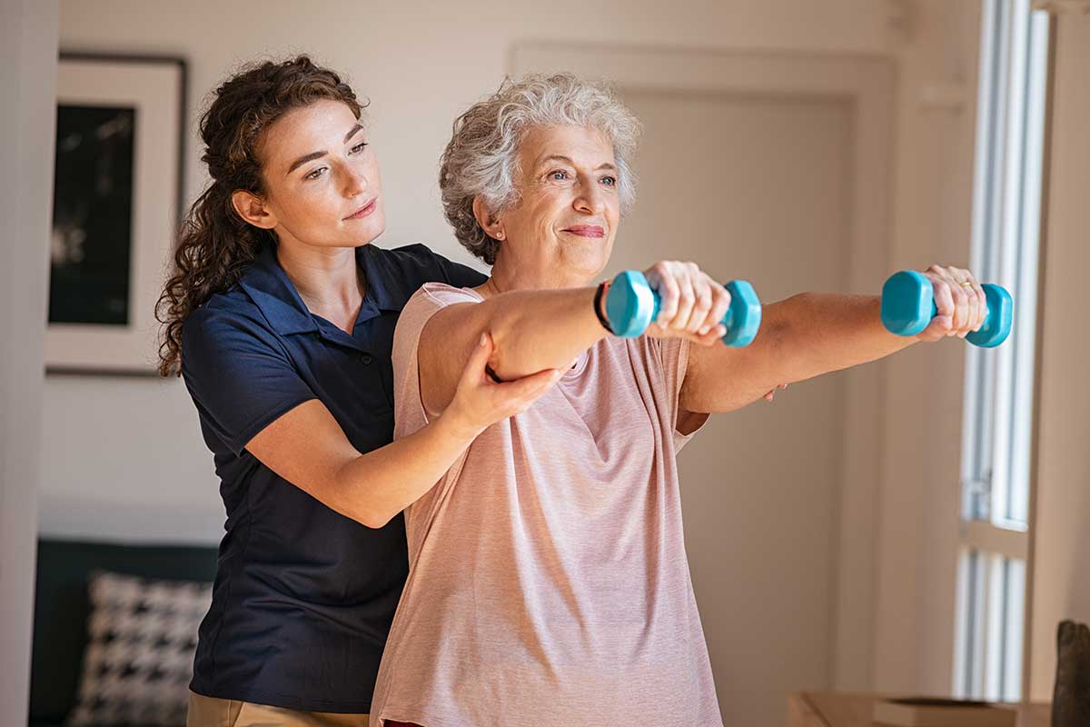 A young female physiotherapist assisting an elderly female client with an arm workout.