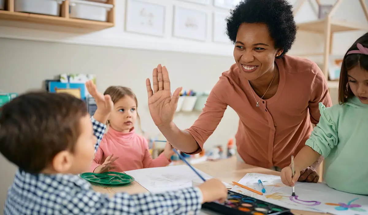 A daycare provider smiles and gives one of her students a high five.