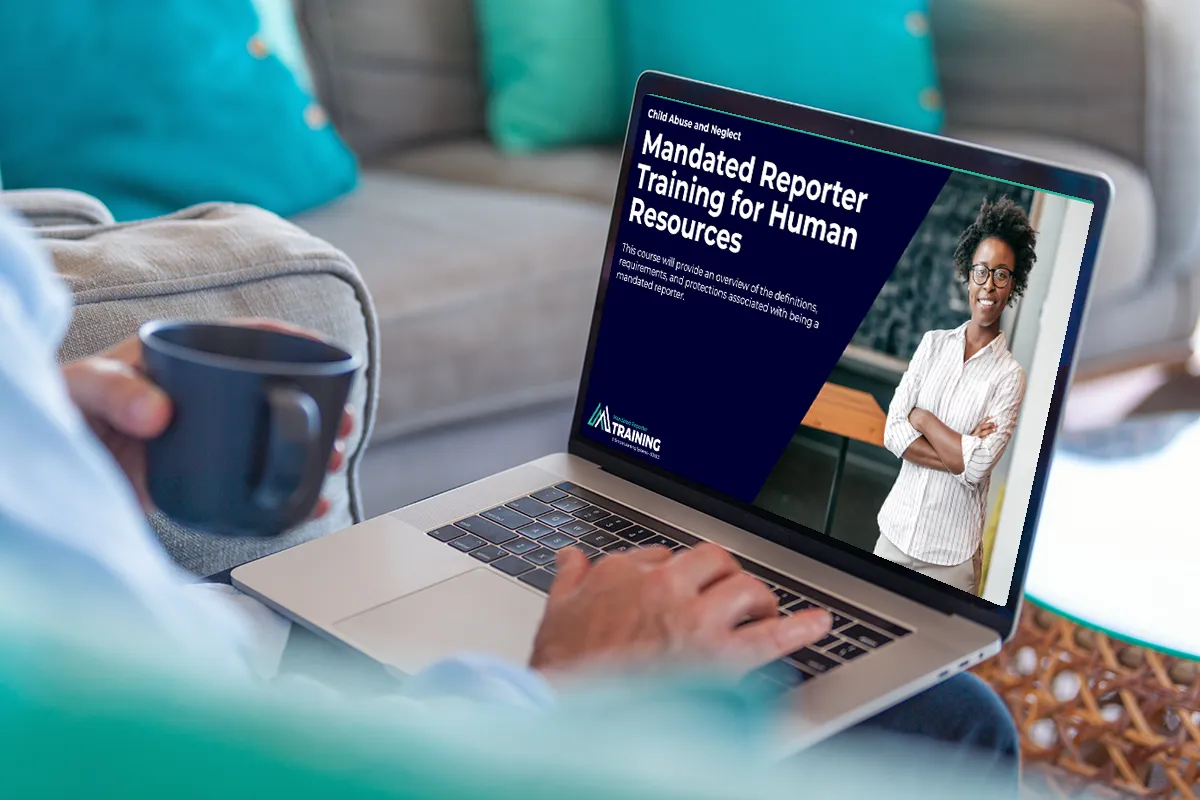 Man holding coffee looking at the computer screen with Mandated Reporter Training pulled up