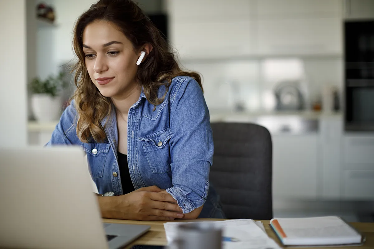 A woman sits at a laptop computer with wireless headphones while she takes an online training at the Mandated Reporter Training platform.