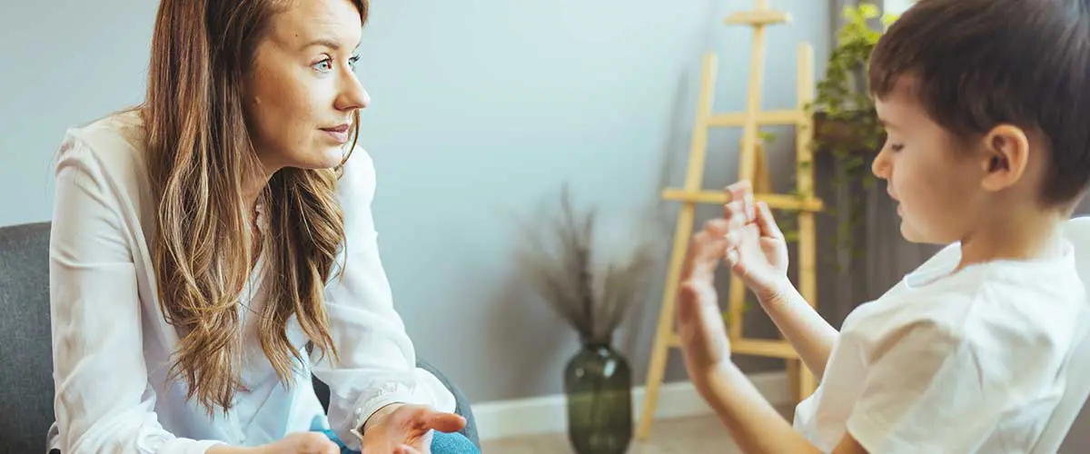 A behavioral analyst listening to a young boy. The boy gestures with his hands while speaking.