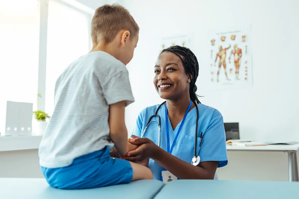 A medical professional is smiling and treating a young patient. They are in a doctor's office.
