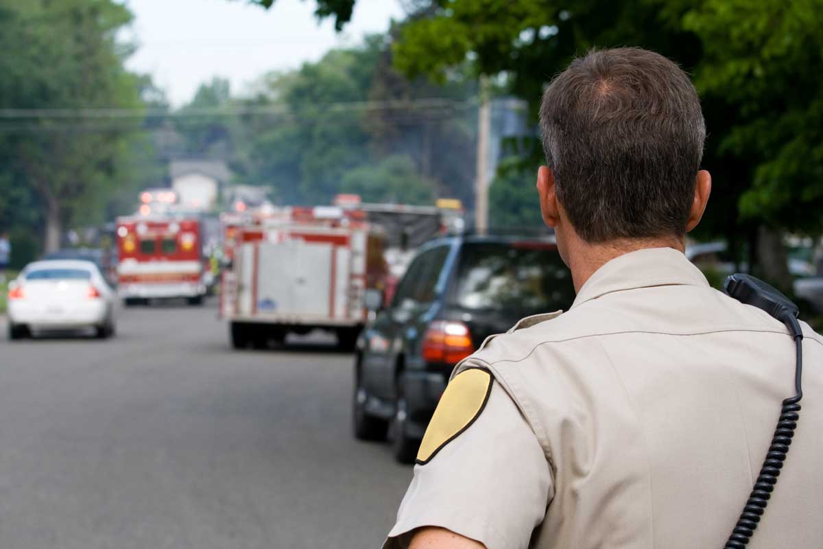 A law enforcement officer looks on at two fire trucks parked in the middle of the street.